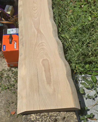 Longue planche brute à bord naturel, posée dehors sur un muret