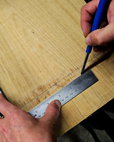 Main traçant une courbe au crayon sur une planche, le long d'un réglet en métal