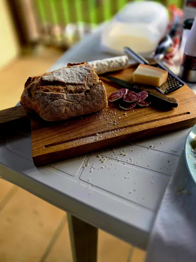 Planche de service garnie de pain, de saucisson et de fromage, sur une table de jardin