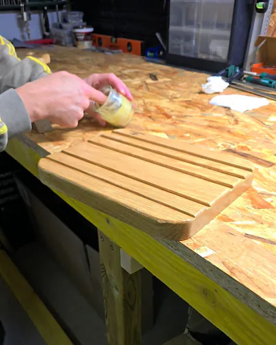Jérémy prend une noisette de baume au doigt dans le pot, au-dessus d'une planche en chêne à rainures