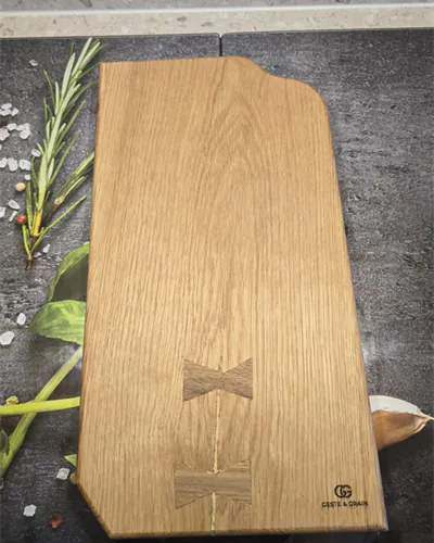Planche de service en chêne avec papillons en noyer, posée sur un plan sombre avec du romarin