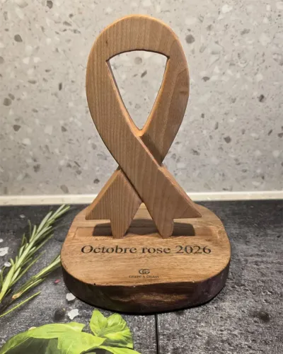 Trophée Octobre rose 2026 en forme de ruban noué, en frêne massif, posé sur un socle en noyer gravé